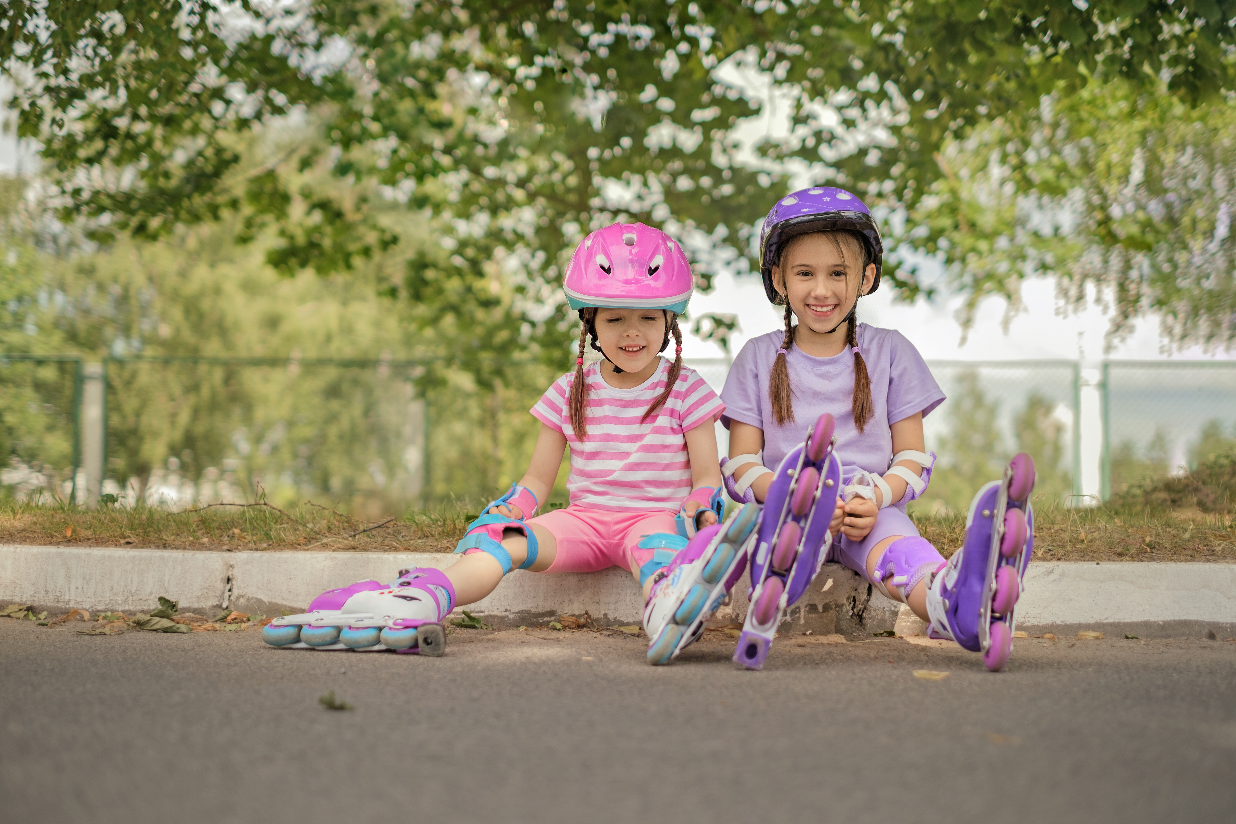 Sisters in protective sports uniforms are sitting resting after roller skating